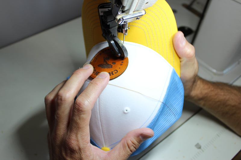 Sewing a round full-grain leather patch onto a yellow and white trucker cap on an industrial sewing machine
