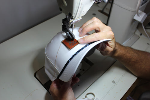 A leather patch sewn onto a white rope cap, stitch line visible around the edge