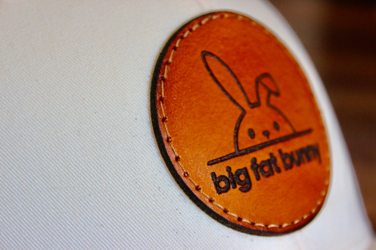 Close-up of an oval full-grain leather patch sewn onto a white cap, laser engraved with a customer's logo